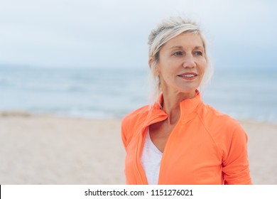 Attractive older blond woman with a thoughtful expression standing on a beach looking to the side with copy space - Powered by Shutterstock