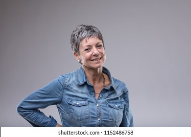 Attractive Older Woman With A Friendly Smile Standing With Hand On Hip Looking Thoughtfully At The Camera Over Grey With Copy Space