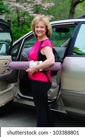 An Attractive Older Woman Holds A Yoga Mat Under Her Arm As She Gets Into A Car.