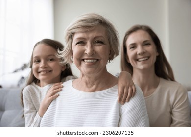 Attractive optimistic mature 60s woman looks at camera pose for picture with lovely granddaughter and young adult daughter. Caucasian female relatives feel happy, portrait of intergenerational family - Powered by Shutterstock