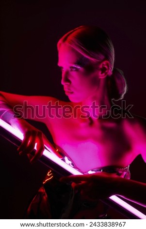 attractive peculiar woman in metallic futuristic attire holding pink LED lamp stick and looking away