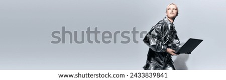 attractive peculiar woman in robotic clothing posing in motion with laptop and looking away, banner