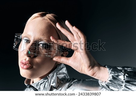 attractive peculiar woman in sci fi glasses and silver attire looking at camera on dark backdrop