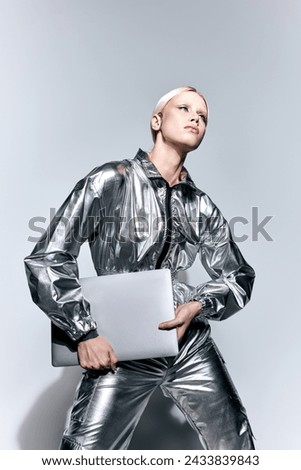 attractive peculiar woman in silver robotic clothing posing in motion with laptop and looking away