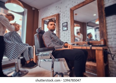 Attractive pensive man is waiting for his turn to get a haircut at busy barbershop. - Shutterstock ID 1396785047