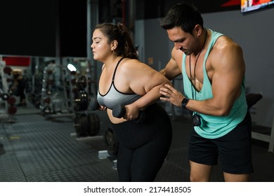 Attractive Personal Trainer Helping An Overweight Young Woman During Her Workout Exercises At The Gym 