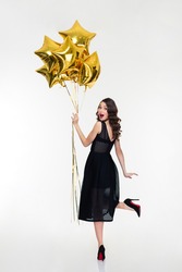 Attractive Playful Happy Woman With Retro Hairstyle In Classic Black Dress And Shoes Looking Back And Holding Golden Balloons