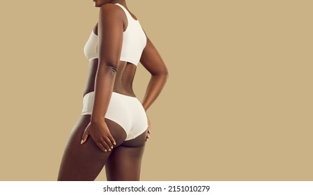 Attractive plus size black woman in underwear. Hot brown skinned model wearing comfy natural cotton undies holding hands on thighs standing on color background. Female body concept, rear back view