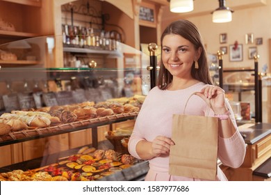 Attractive plus size woman smiling to the camera, holding paper shopping bag, copy space. Happy woman shopping at the bakery store - Powered by Shutterstock