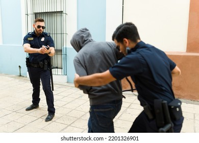 Attractive Police Officer Pointing His Gun To A Criminal While His Partner Making An Arrest And Putting Handcuffs