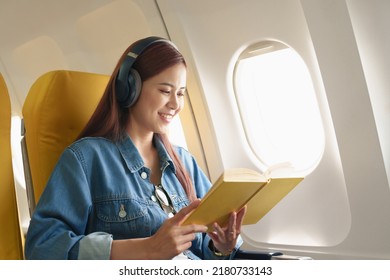 Attractive portrait of an Asian woman sitting in a window seat in economy class reading a book and listening to instrumental music during an airplane flight, travel concept, vacation, relaxation - Powered by Shutterstock