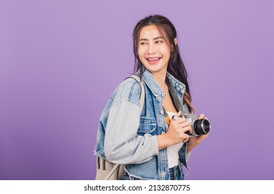 Attractive portrait happy Asian beautiful young woman smiling excited wear denims and bag holding vintage photo camera, female traveler female photographer, studio shot isolated on purple background