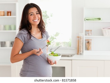 Attractive pregnant woman holding a bowl of salad while standing in the kitchen