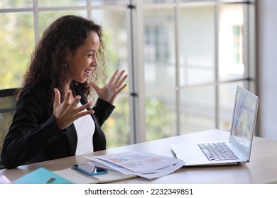 Attractive professional latin female employee worker sitting, using laptop computer with smart mobile phone at home workplace. Businesswoman working on paperwork while looking at camera and smile - Shutterstock ID 2232349851