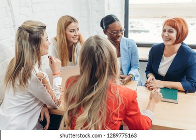 Attractive Red-haired Female Teacher Speaking To A Group Of Young Student Girls At Training Seminar, All Women Dressed In Casual Colorful Jackets.