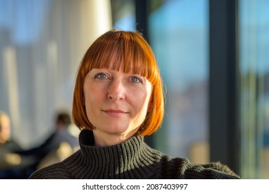 Attractive redhead woman with lovely twinkling blue eyes looking at the camera with a quiet friendly smile indoors in a close up head shot