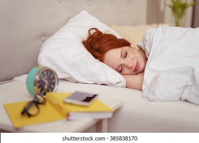 Attractive redhead woman sleeping in bed with a serene smile on her face and an alarm clock on the table alongside - Powered by Shutterstock