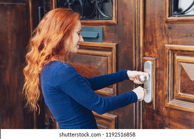 Attractive redhead woman unlocking a large old wooden front door with her key in a close up profile portrait