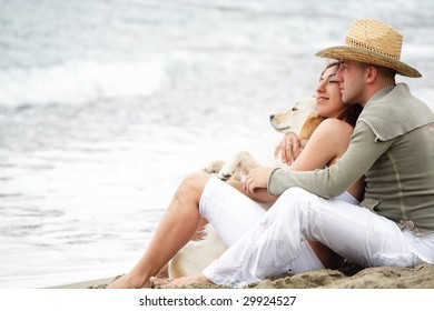 Attractive Romantic Couple With A Dog Sitting On The Beach