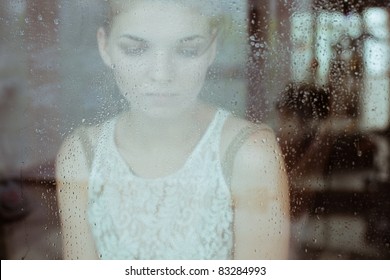 Attractive Sad Girl Standing At The Window Watching The Rain