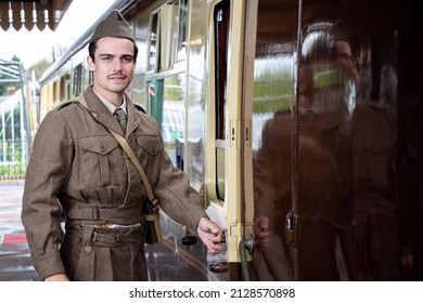 Attractive And Sad Male British Soldier In Vintage WW2 Uniform At Train Station Standing Next To Train