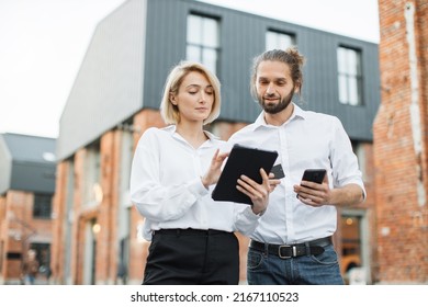 Attractive satisfied business couple standing outdoors near office building and making online payment using credit card, tablet and smartphone. Checking account balance, buying of goods concept. - Powered by Shutterstock