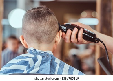 Attractive school boy is getting trendy haircut from mature hairdresser at fashionable hairdressing salon.