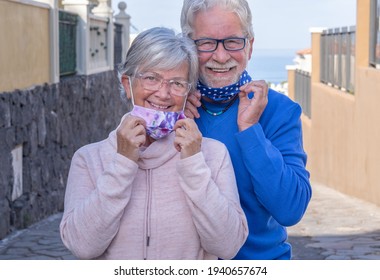 Attractive senior couple already vaccinated against coronavirus contagion - smiling outdoors taking off protective masks - Shutterstock ID 1940657674