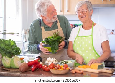 Attractive senior couple preparing vegetables together in the home kitchen laughing amused. Caucasian elderly people enjoying healthy eating - Powered by Shutterstock