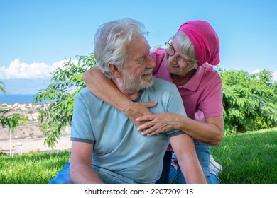 Attractive Senior Couple Sitting In The Meadow During Summer Vacation Embracing With Love. Elderly People Enjoying Retirement And Free Lifestyle