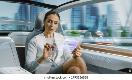 Attractive Senior Female Reading News on a Futuristic Transparent Tablet Computer with Augmented Reality Interface while Sitting on a Backseat of Autonomous Car. Self-Driving Van Rides on Public Road. - Powered by Shutterstock