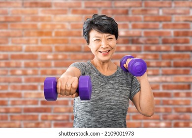 Attractive Senior Fitness Asian Woman Exercise And Training. Elder Exercising At Home Gym Or Fitness With Dumbbells Over Red Bricks Wall Background. Active Older Exercise And Workout Concept.