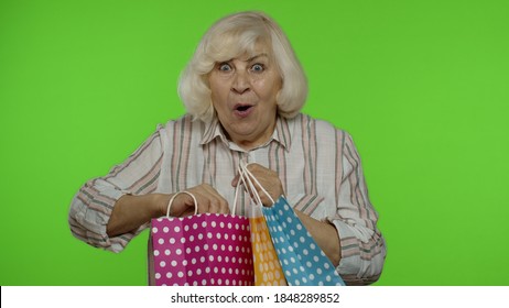 Attractive Senior Grandma Raising Shopping Bags, Celebrating, Looking Satisfied With Purchase, Enjoying Discounts On Black Friday Holiday. Elderly Woman Isolated On Chroma Key Background