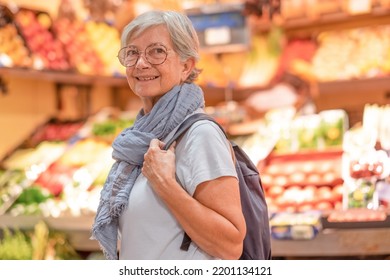 Attractive Senior Woman With Backpack And Scarf Walking For Shopping At The Farmer Market Looking For Fresh Fruit And Vegetables