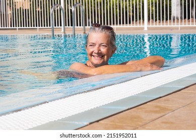 Attractive senior woman relaxing outdoors in the swimming pool enjoying sun and vacation. Elderly woman swimming alone in the blue water enjoying healthy lifestyle and retirement