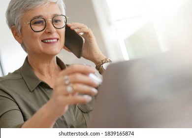 Attractive senior woman talking on phone in office - Powered by Shutterstock