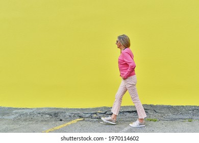 Attractive senior woman walking against brightly colored yellow wall outdoors