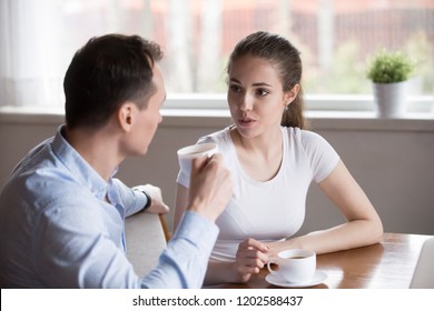 Attractive Serious Millennial Couple In Love Sitting In Kitchen Drinking Morning Coffee At Home. Young Childfree Wife And Husband Talking About Upcoming Work Day Or Discussing About Plans On Weekend