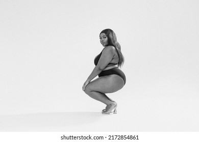 Attractive Sexy Dark Skinned Woman In Black Fashionable One Piece Swimsuit, Looking At The Camera. Full Photo Of Superb Plus Size Girl Posing In Studio On The Gray Background. Copy Space. 