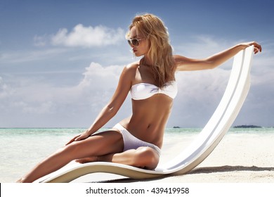 Attractive and sexy girl on the beach. fashion photo of beautiful tanned woman with blond hair in elegant White bikini relaxing in beach chair 