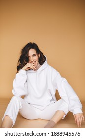 Attractive sexy woman wear white total look. Girl look sexy and happy. Elegant look. Brunette model sitting in white hoody and jeans. Winter, fall autumn or spring minimal outfit. Woman is positive.