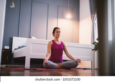 Attractive shape sporty middle aged woman doing seated yoga poses on the floor before sleeping.