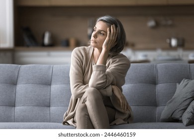 Attractive silent middle-aged woman relaxing seated on couch in living room, staring out window, ponders, missing, deep in thoughts, looks pensive and thoughtful, spend boring weekend alone at home - Powered by Shutterstock