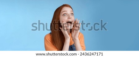 Attractive silly european redhead young girl 20s calling friend searching someone crowd look relaxed joyfully yelling hold hands opened mouth shouting name louder look left, blue background.