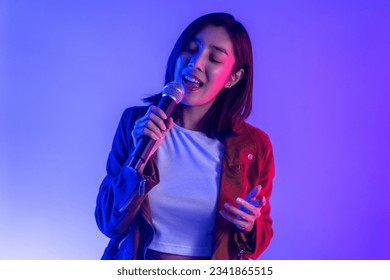 Attractive singer woman singing music on stage with spotlight strike through the darkness at concert event. Musician performing live with neon light in hall.
