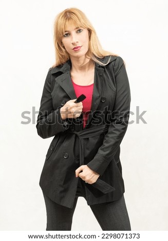 attractive slim Caucasian middle-aged blonde girl tying a knot with the ribbon of her black coat in a photo studio against a white background