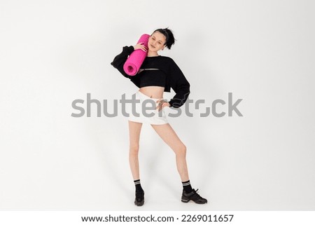 Attractive Slim Girl wearing black short top and white mini skirt, Posing and holding rolled up yoga mat. Isolated on white background.