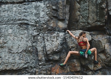 attractive slim muscular young woman rockclimber climbing on tough sport route on granite cliff, resting and chalking hands. outdoors rock climbing, exercising and active lifestyle concept. 