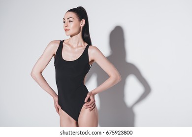 Attractive slim woman in black leotard posing with hands on waist and looking away