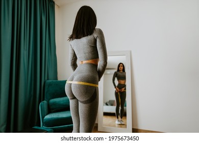 attractive slim Woman Measuring body With Tape Standing In Front Of Mirror At Home. Beautiful woman checking success of weight loss program and measuring butt and hips in front of mirror in living